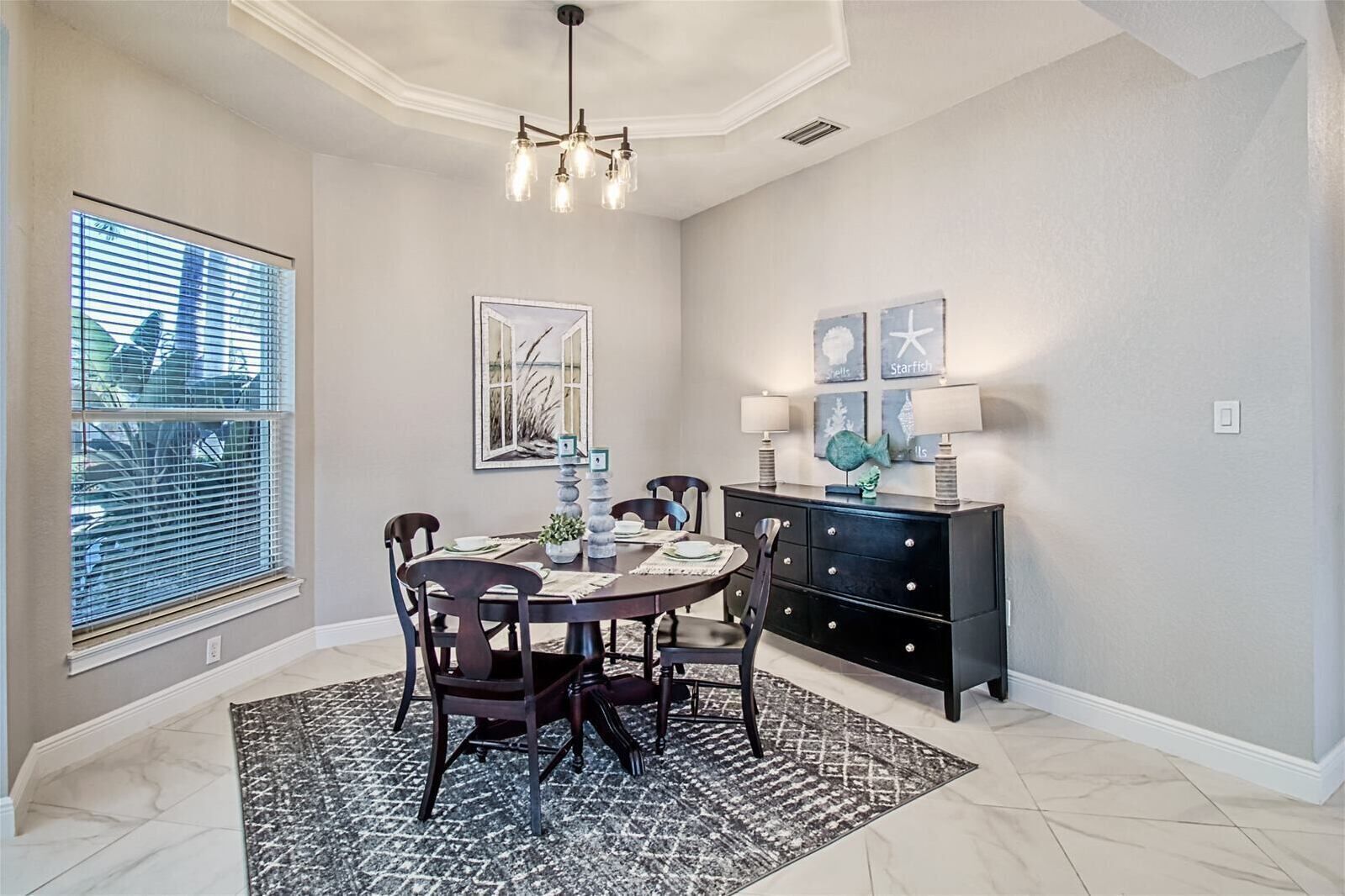 A dining area with a round table, chairs, a black cabinet, and artwork on the wall.