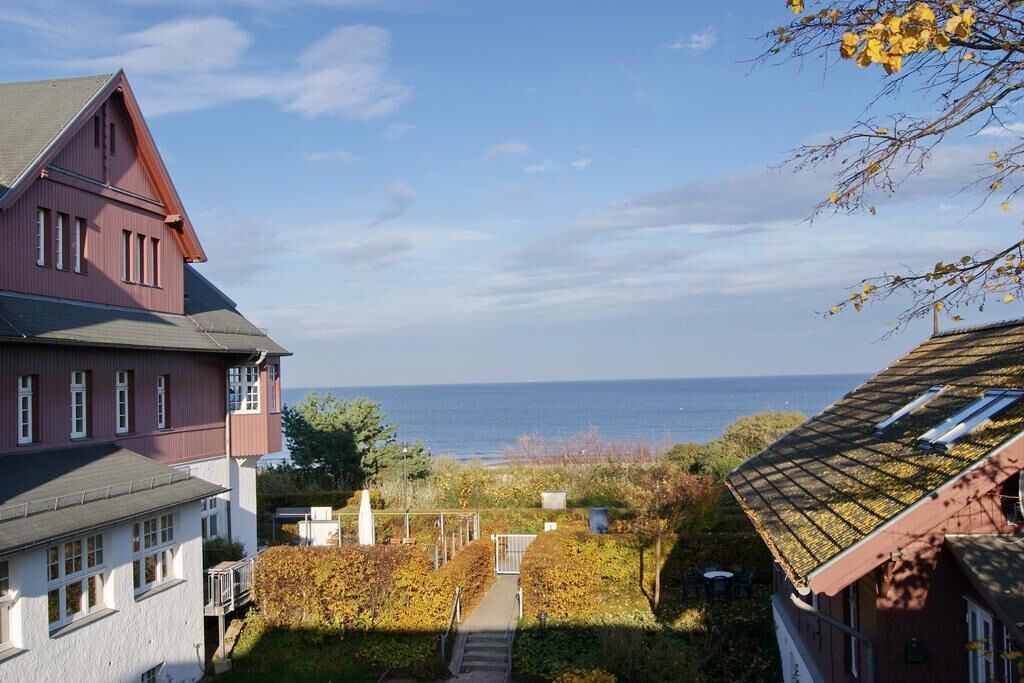 A coastal property with a view of the sea, a pathway leading to a gate, and a garden with autumn foliage.