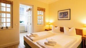 Une chambre d’hôtel avec deux lits, une fenêtre avec des rideaux, un tableau encadré au mur et une petite table avec une lampe.
