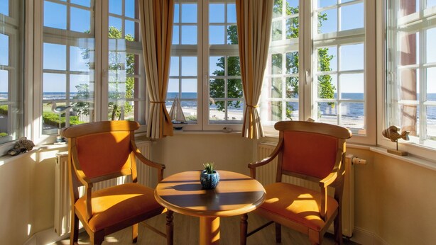 Une pièce dotée d’une grande fenêtre en saillie offrant une vue panoramique, de deux chaises en bois, d’une petite table et d’une plante en pot.