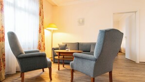 A living room with two armchairs, a sofa, a small wooden table, and a floor lamp.
