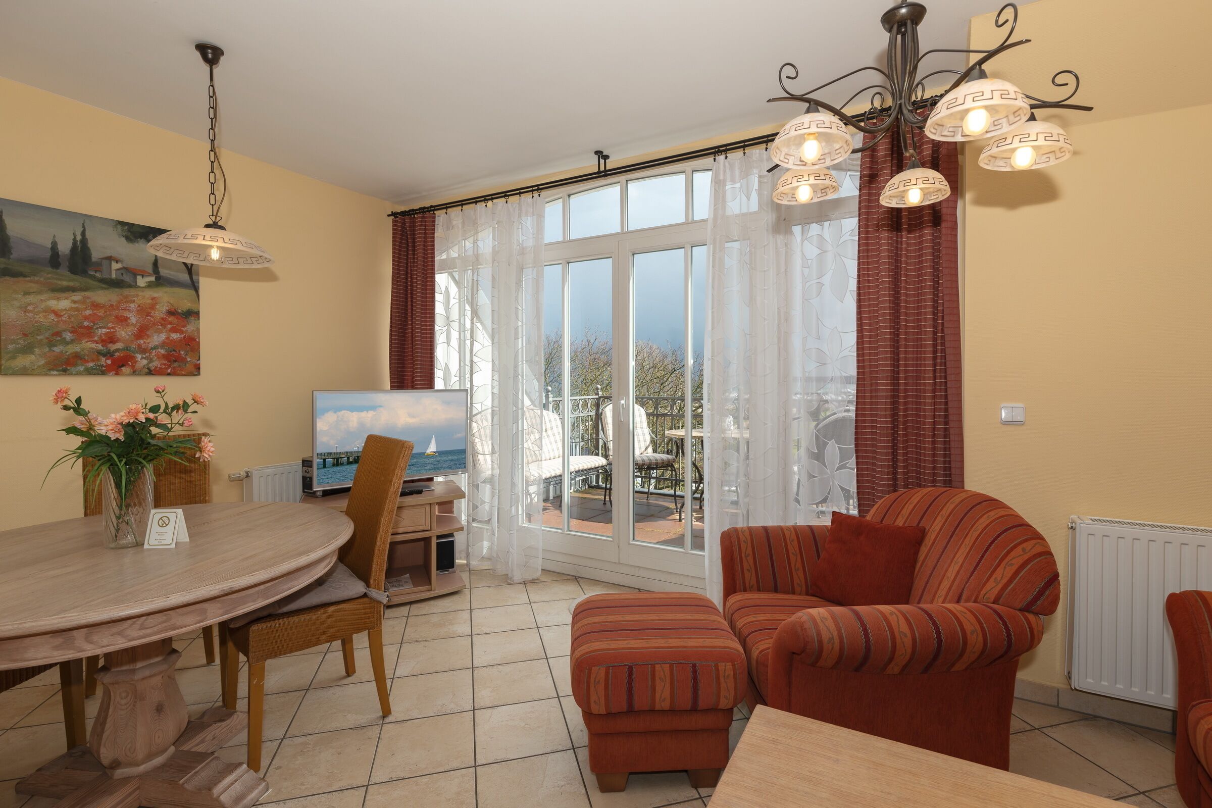 A dining area with a round table, chairs, and a TV. There are two sofas and a window with curtains.