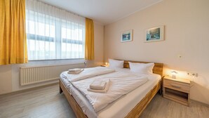 A hotel room with a large bed, two bedside tables, a nightstand, and a window with curtains.
