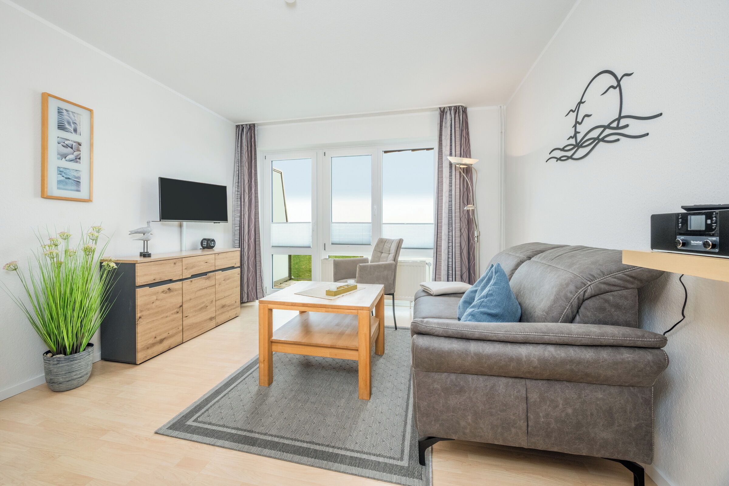 A modern living room with a sofa, a coffee table, a TV, and a view of the sea.