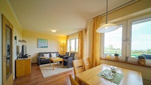 A modern living room with a sofa, a dining table, and a TV. - Strandnahe, Lichtdurchflutete Ferienwohnung an der Nordsee mit Meerblick u. Wlan (Nordseeheilbad Schillig)
