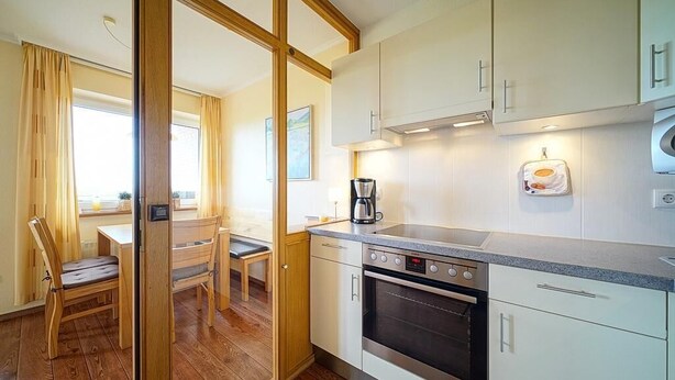 A compact kitchen with a built-in oven, a coffee maker, and a microwave. There is a dining area with a table and chairs. - Strandnahe, Lichtdurchflutete Ferienwohnung an der Nordsee mit Meerblick u. Wlan (Nordseeheilbad Schillig)