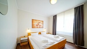 A hotel room with a large bed, bedside tables, a painting, and a window with curtains. - Strandnahe, Lichtdurchflutete Ferienwohnung an der Nordsee mit Meerblick u. Wlan (Nordseeheilbad Schillig)