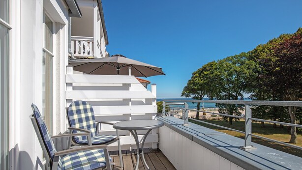 A balcony with a table and chairs, a white railing, and a view of the sea.