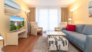 A modern living room with a flat-screen TV, two armchairs, a sofa, a coffee table, and a patterned ottoman.