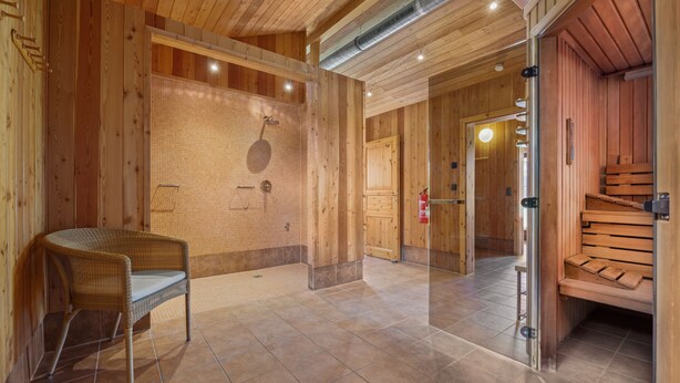 A wooden interior with a shower area, a wicker chair, and a sauna.