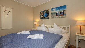 A neatly made bed with white linens and a blue patterned bedspread, two bedside lamps, and wall art depicting beach scenes.
