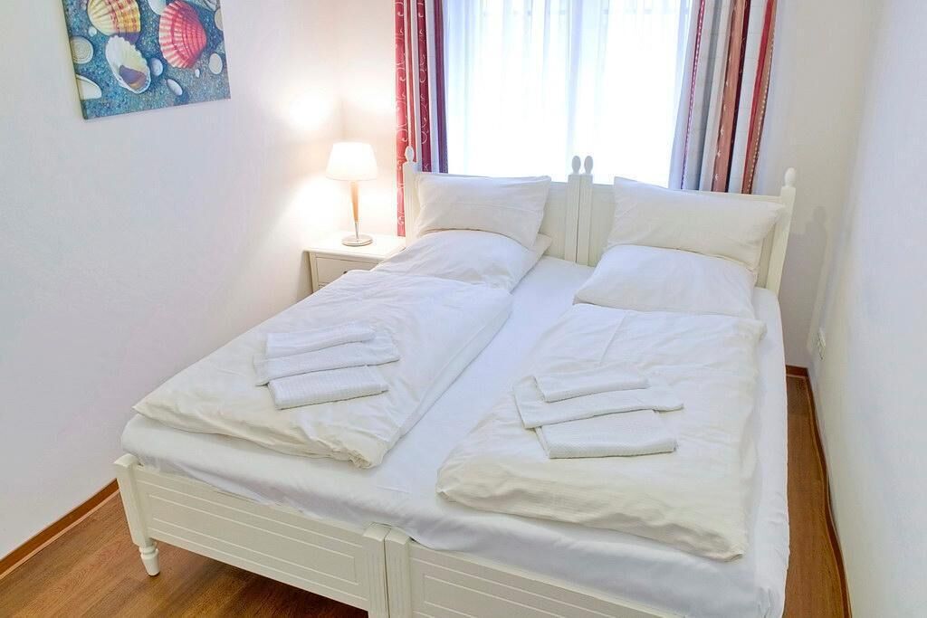 A neatly made double bed with white linens and towels, a bedside lamp, and a wall with a seashell painting.