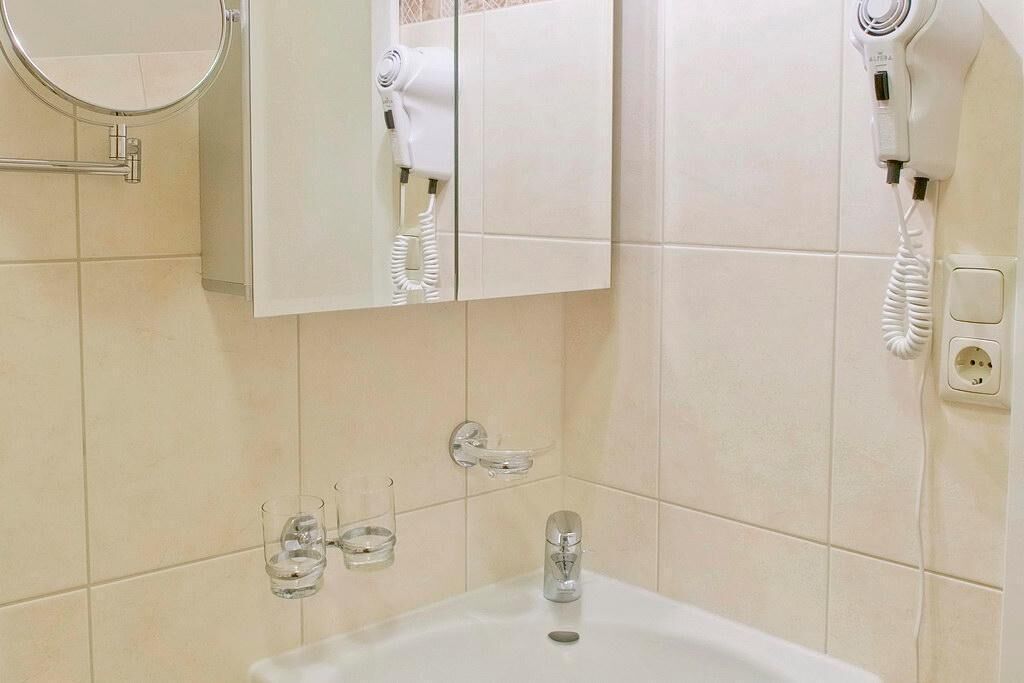 Een badkamer met een witte wastafel, een spiegel, een haardroger en een handdoekhouder.