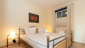 A neatly made bed with white linens, a bedside lamp, and a framed picture on the wall.