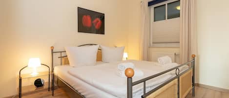 A neatly made bed with white linens, a bedside lamp, and a framed picture on the wall.