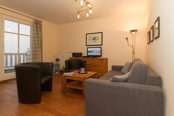 A living room with a sofa, armchair, and a wooden coffee table. There is a television on a stand and a floor lamp.