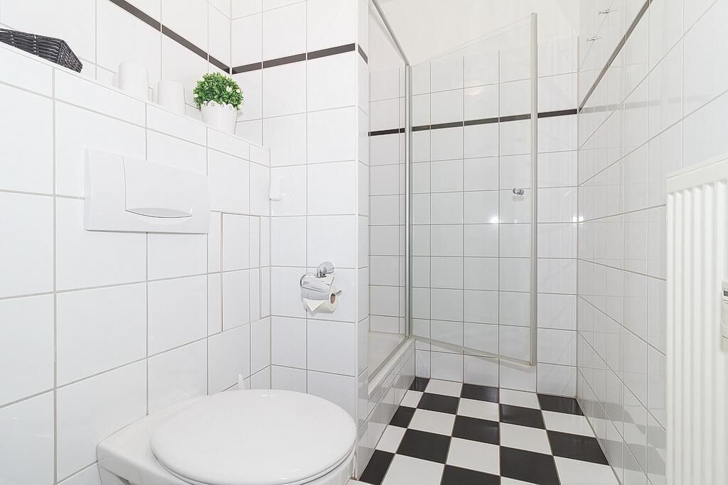 Un bagno con piastrelle bianche, un water, una doccia con pareti in vetro e un pavimento a scacchi bianco e nero.