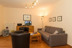 A living room with a sofa, two chairs, a coffee table, a TV, a radiator, and framed pictures on the wall.