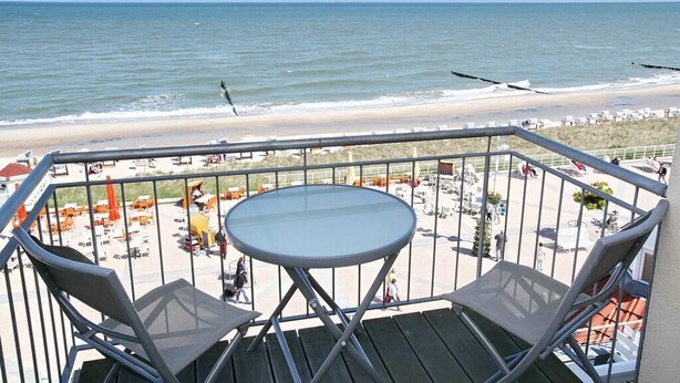A balcony with a table and chairs overlooking a beach.