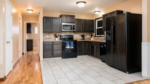 A kitchen with dark wooden cabinets, a stainless steel microwave, a black refrigerator, and a tiled floor. - Comfortable Pet friendly (Albany)