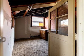A narrow, dimly lit room with a single window, a radiator, and a door.