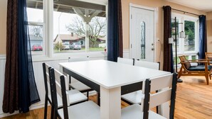A dining area with a white table and chairs, large windows with curtains, and a view of the outside. - Comfortable Pet friendly (Albany)