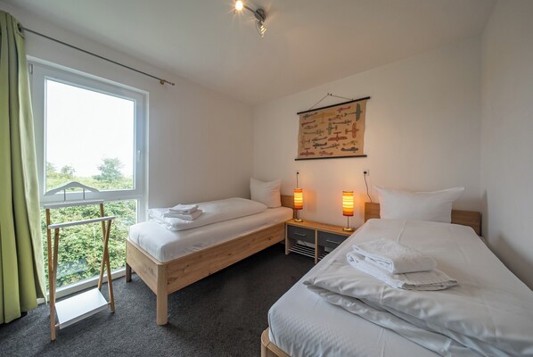 A hotel room with two beds, a window with curtains, a wall-mounted artwork, and bedside lamps.