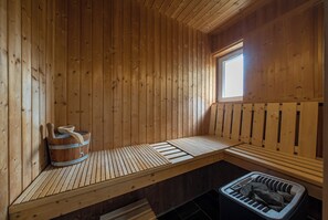 A wooden sauna with benches, a window, and a wooden bucket.