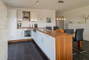 Eine moderne Küche mit weißen Schränken, einer Holz Arbeitsplatte und einem eingebauten Backofen. Es gibt einen Essbereich mit einem Holztisch und schwarzen Stühlen.