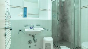 Un baño con lavamanos blanco, espejo y cabina de ducha con paredes de vidrio.