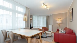 A modern living room with a dining table, red sofa, and a large window with sheer curtains.