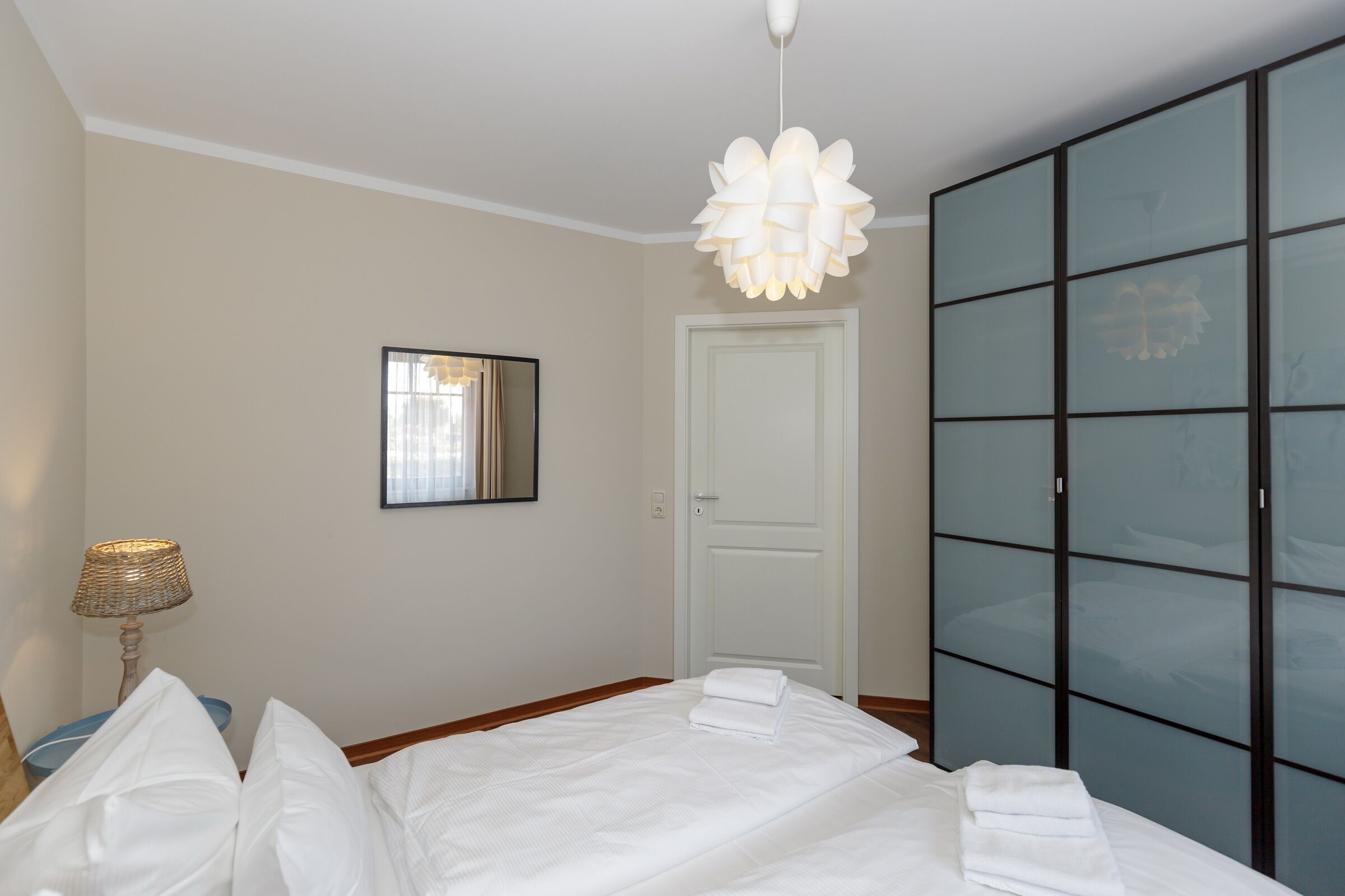 A hotel room with a bed, a bedside lamp, a wardrobe, and a hanging light fixture.