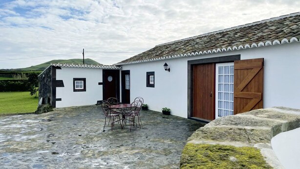 Un edificio blanco con techo de tejas, una puerta de madera y un muro de piedra.