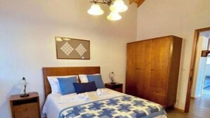 Un dormitorio con techo de madera, una cama con cubrecama estampado, una mesita de noche, un armario y un aplique de pared.