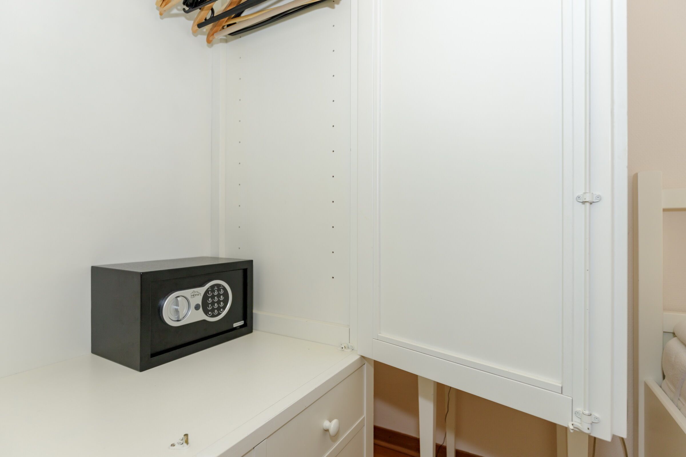 A white wardrobe with a small safe on the top shelf.