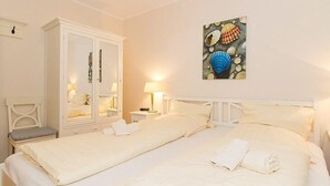 A hotel room with two beds, a wardrobe, a bedside table with a lamp, and a wall-mounted artwork of seashells.