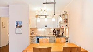 Une cuisine moderne avec des meubles blancs, une table à manger en bois et des luminaires suspendus.