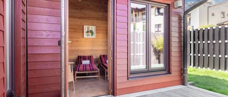 A wooden cabin with a sliding glass door, a small porch, and a bench inside.