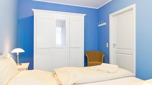Une chambre avec deux lits, une armoire blanche, une chaise et une table de chevet avec une lampe.