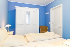 Ein Schlafzimmer mit zwei Betten, einem weißen Kleiderschrank, einem Sessel und einem Nachttisch mit Lampe.