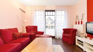 Un salon avec des meubles rouges, une table basse en bois et un téléviseur posé sur un meuble blanc.