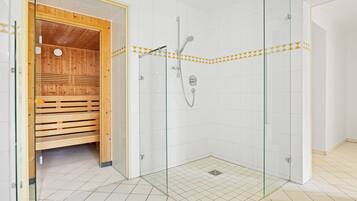 A modern bathroom with a glass-enclosed shower, wooden sauna, and tiled floor.
