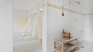 Ein modernes Badezimmer mit weißen Fliesen, einer Holzbank, einem Holzeimer und einer Duschkabine mit Handtuchhalter.