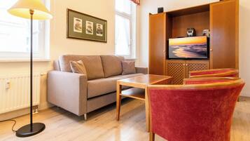Ein Wohnzimmer mit einer Couch, einem Tisch, einem roten Sessel, einem Fernseher und einer Stehlampe.