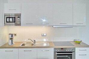 Una cucina moderna con mobili bianchi, un forno a microonde in acciaio inossidabile, una macchina da caffè, un lavello e un forno.