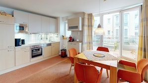 A modern kitchen with white cabinets, a microwave, and a dining area with orange chairs and a table.