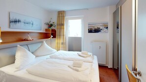A hotel room with two beds, a wooden headboard, a wall-mounted artwork, a radiator, and a view of the sea through a window.
