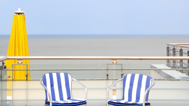 Two striped lounge chairs facing a beach with a yellow structure in the background.