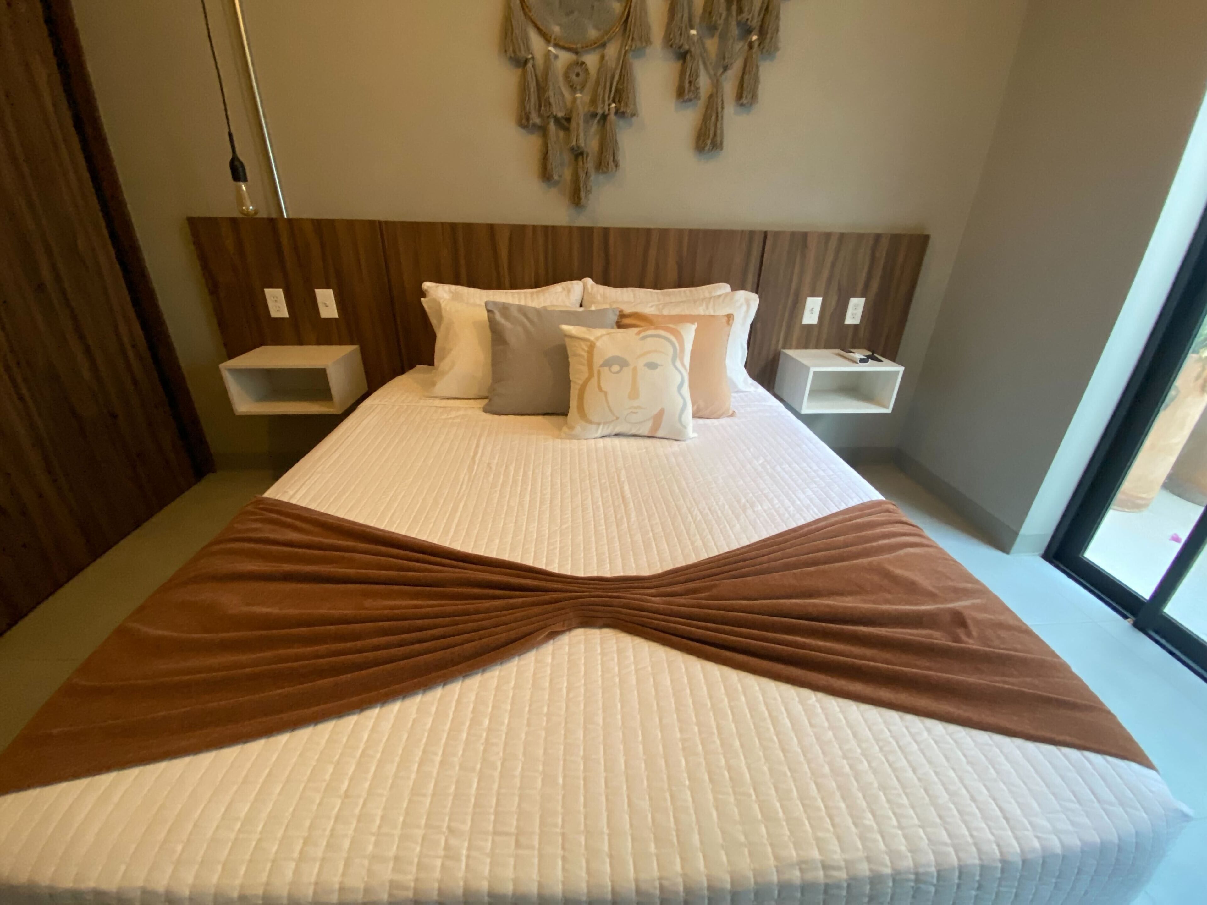A neatly made bed with a brown blanket, white bedding, and a headboard with wall-mounted shelves.