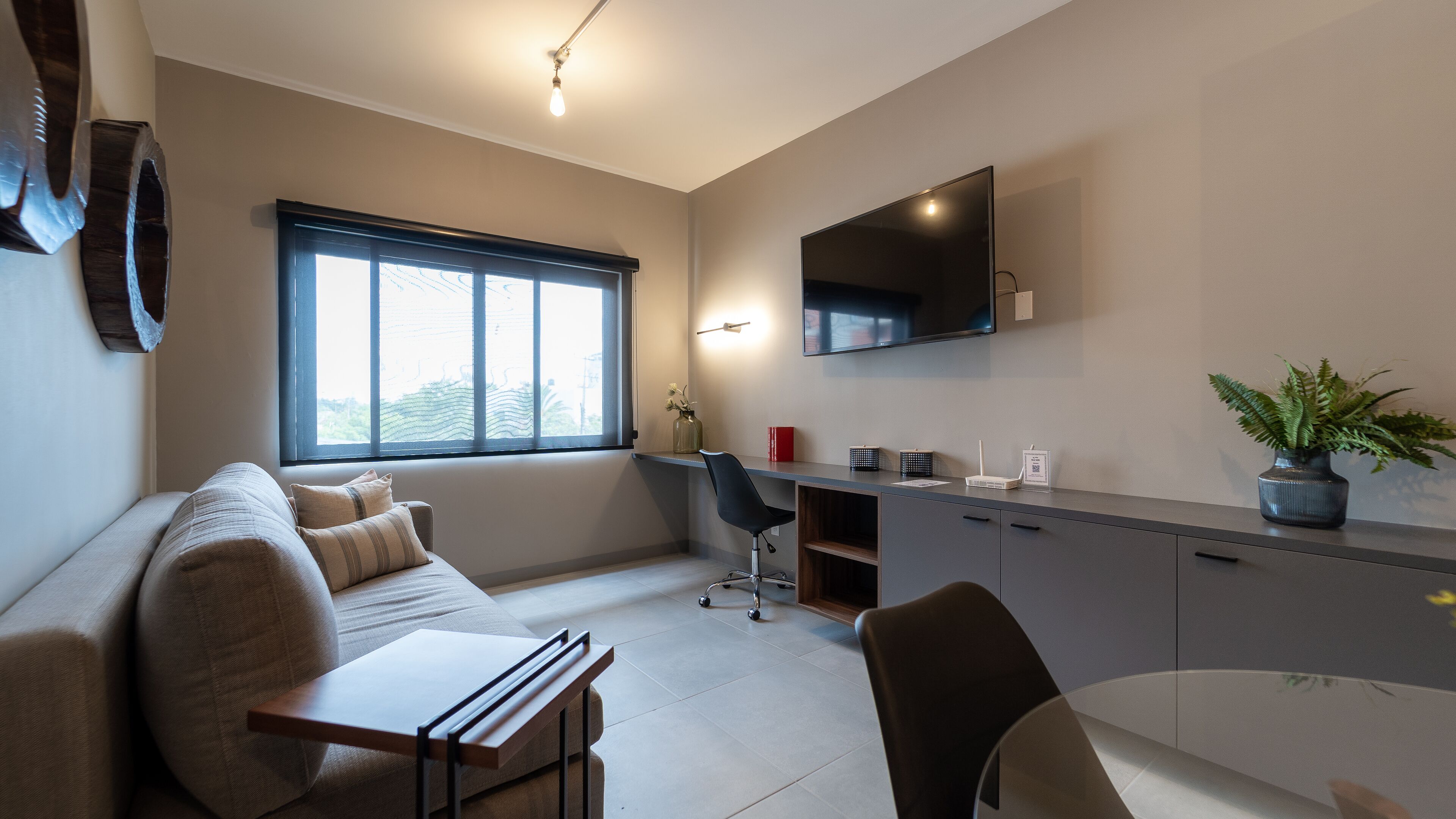 Une pièce moderne et bien éclairée, avec un canapé, un bureau et un téléviseur fixé au mur.